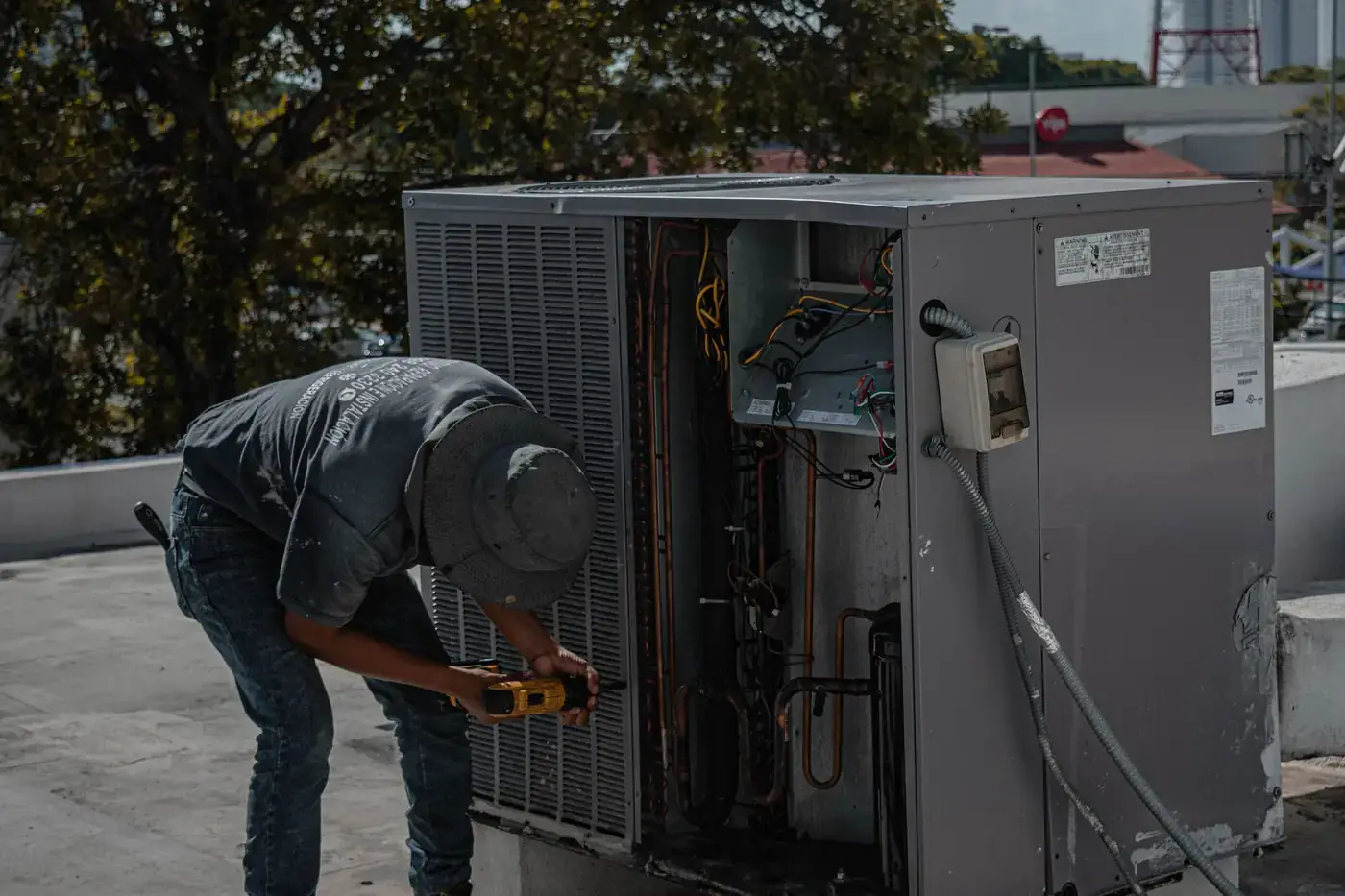Technician working inside an open outdoor air conditioning unit on a flat roof