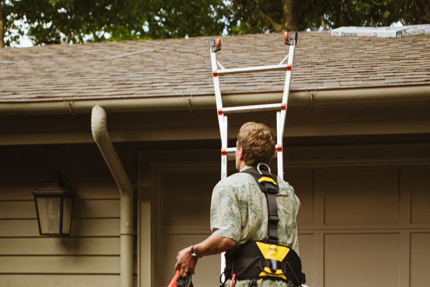 Worker in a safety harness climbing a ladder to the roof of a house