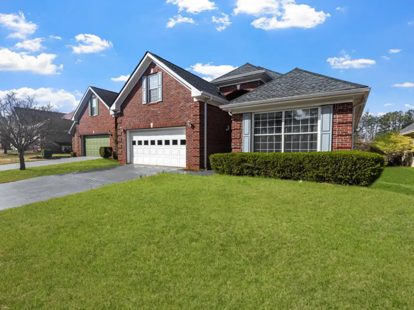 Red brick house with an attached two-car garage and a wide green lawn under a blue sky