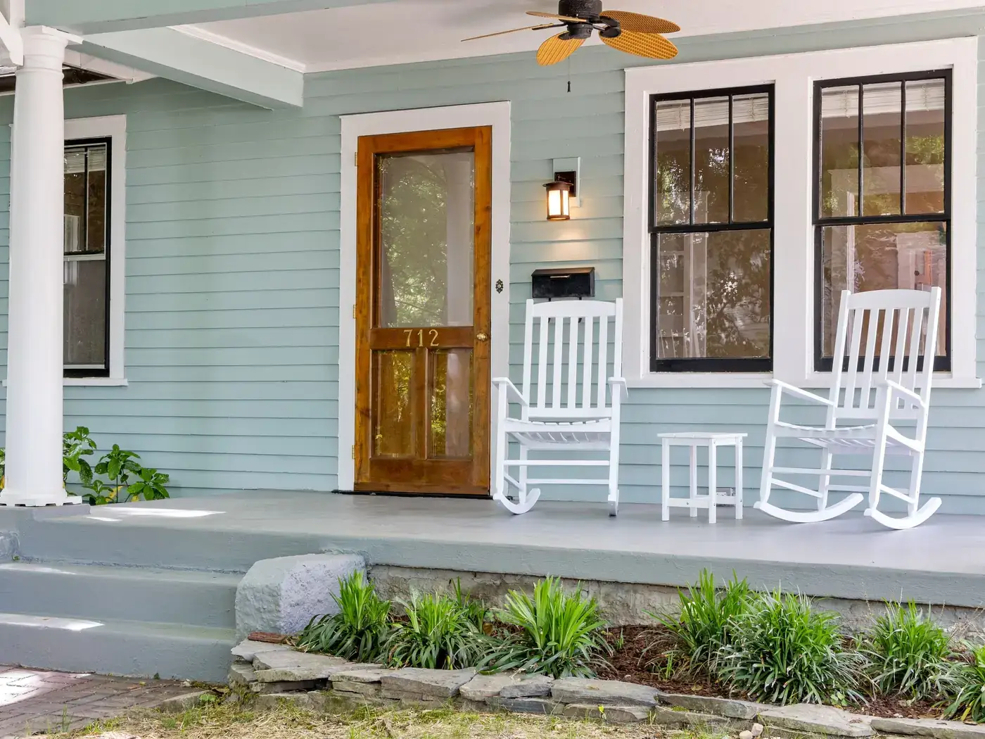 Front porch with white rocking chairs, a wood front door and light blue siding