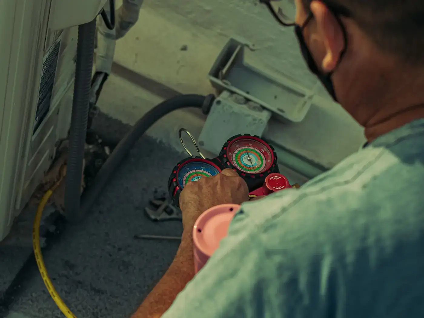 Technician in a face mask reading refrigerant manifold gauges beside an outdoor air conditioning unit
