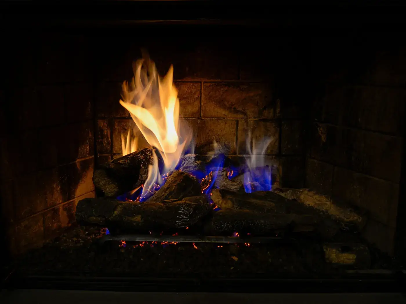 Gas fireplace with ceramic logs burning with orange and blue flames