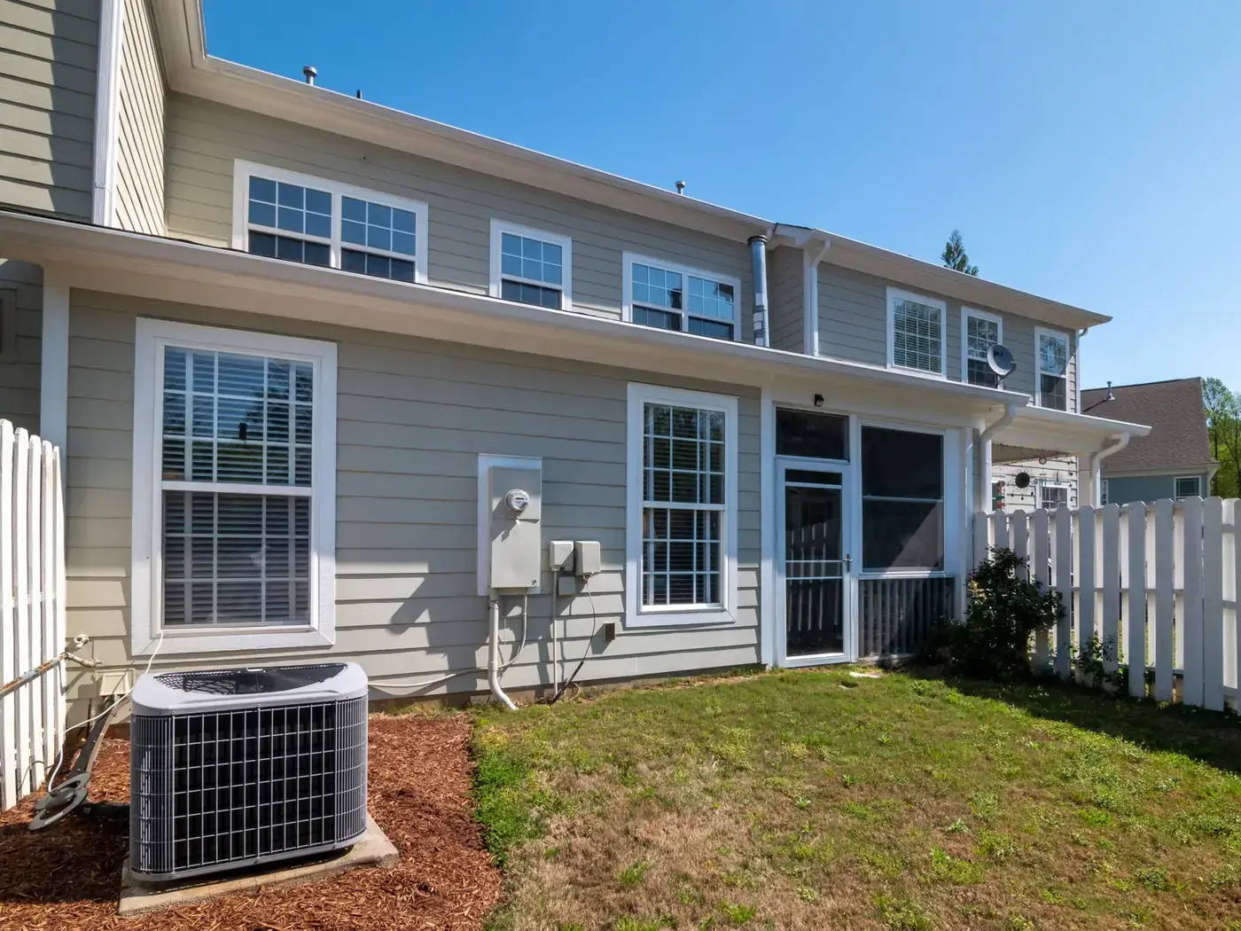 Outdoor air conditioning condenser on a mulch bed behind a two-story house with gray siding