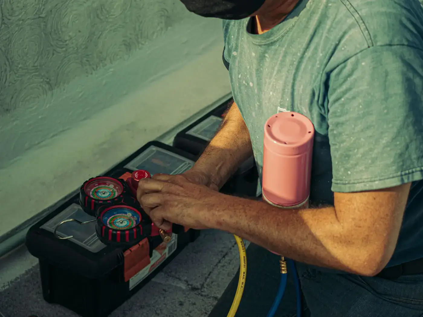 Technician kneeling beside a toolbox and connecting refrigerant gauges during an air conditioning service